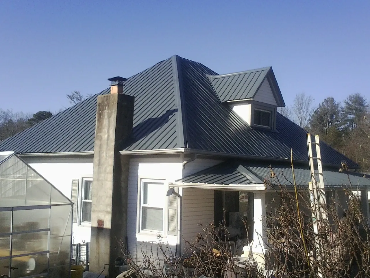 Dark blue standing seam metal roof on a white farmhouse with dormer — Slate & Tile Roof Repair by Roofing Brothers in Buffalo
